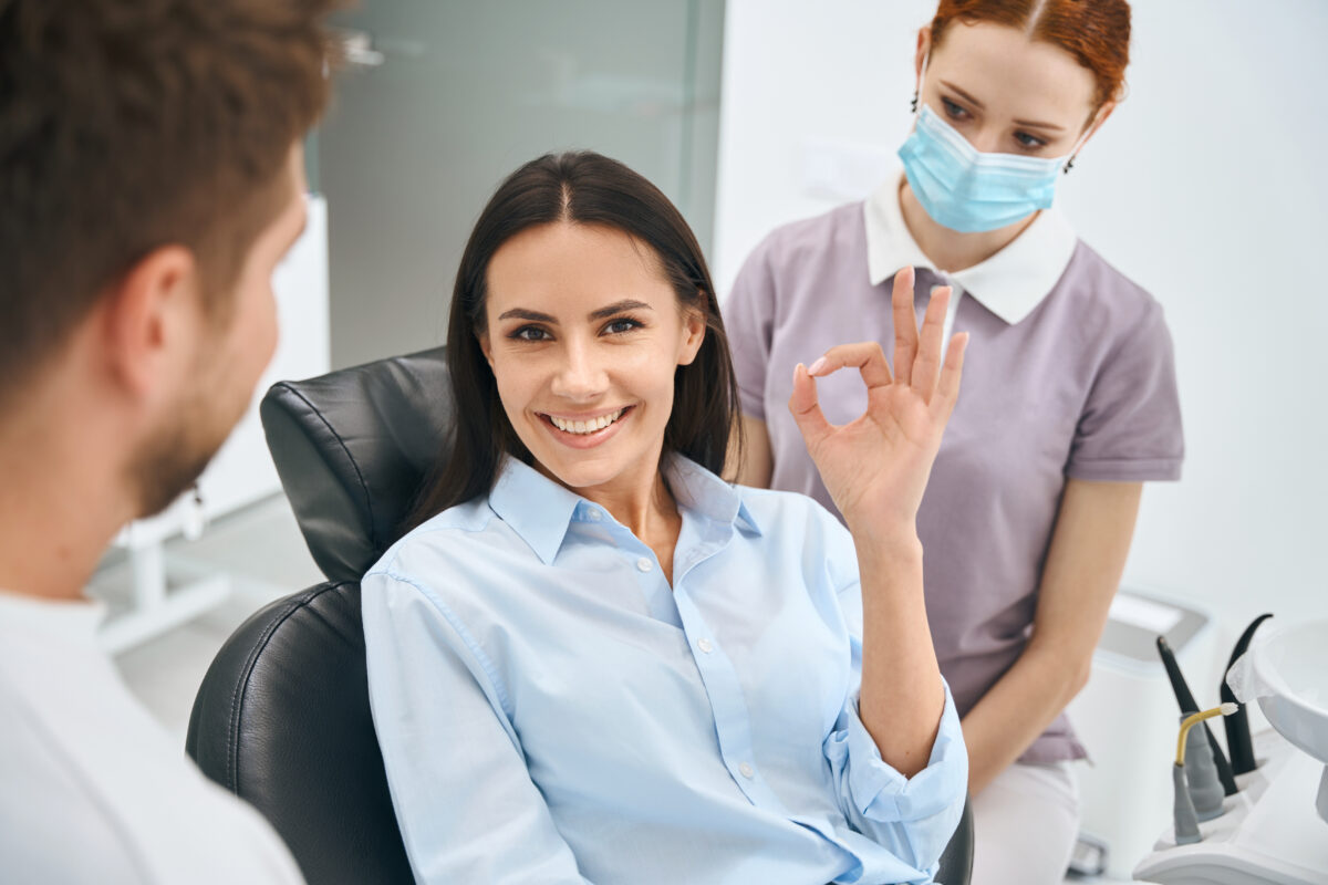 Smiling patient giving an OK sign with the dental team nearby